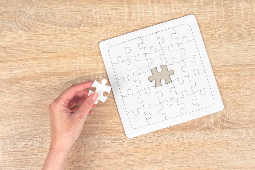 Female hand putting a missing piece into jigsaw puzzle