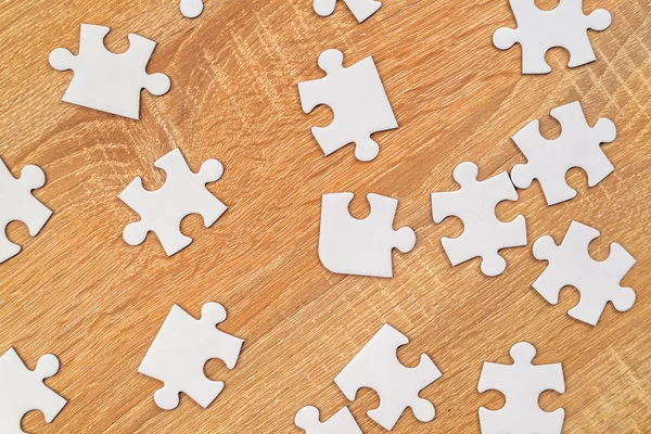 White jigsaw puzzle pieces scattered on wooden table — 스톡 사진