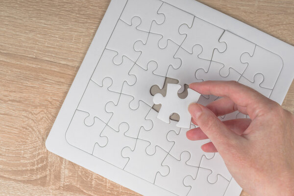 Female hand putting a missing piece into jigsaw puzzle