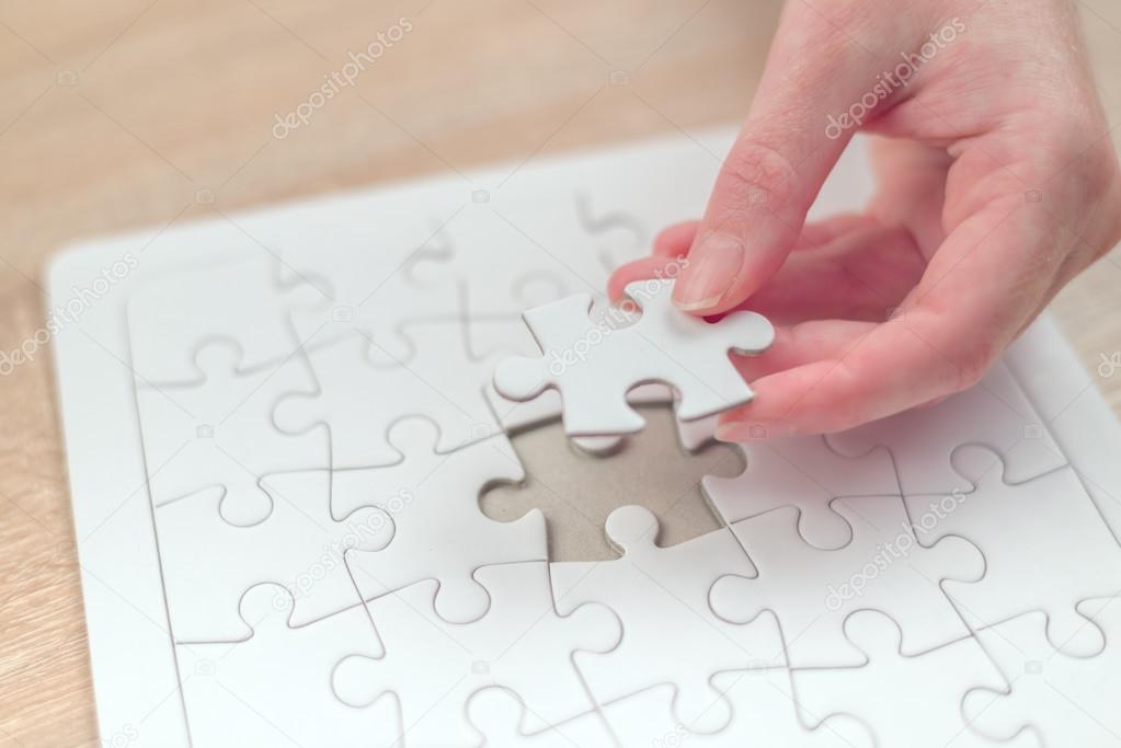 Female hand putting a missing piece into jigsaw puzzle