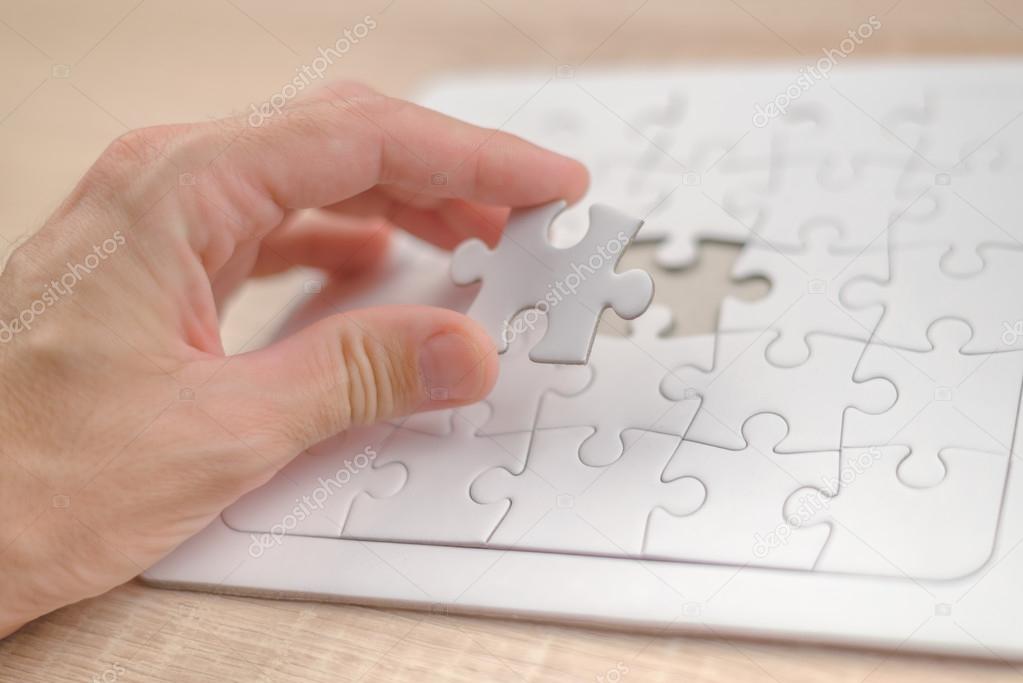 Male hand putting a missing piece into jigsaw puzzle