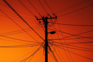 Tangled overhead power cables and street pole in front of a dramatic evening sky. Selective focus.