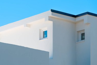 Modern white minimalist building with geometric lines and windows under clear blue sky, contemporary Mediterranean architecture detail. Selective focus.