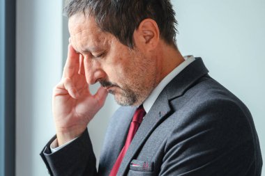 Ofis penceresinin yanında duran yorgun işadamı, elini alnına dayayıp, kurumsal yöneticinin iş sorunlarını düşündüğünü vurguladı. Seçici odak.