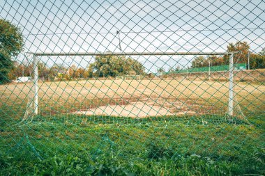 Eski kale direği ve yamalı çimleriyle terk edilmiş bir futbol sahası, oyunun çürüme ve nostaljisini gösteriyor. Seçici odak.