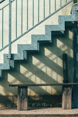 Bir çiftlikte ahşap bank ve metalik merdiven, işlevsel açık hava oturma ve mimari detay içeren kırsal bir sahne. Dikey resim.