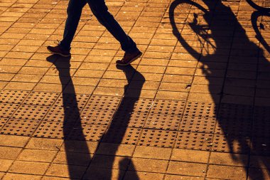 Yaya ve bisiklet gölgeleri sıcak bir akşam ışığında kaldırımda. Seçici odak.