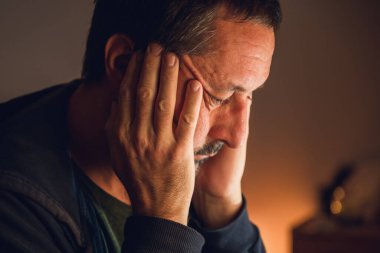 Umutsuzluk ve iç çatışmayı sembolize eden yumuşak sıcak ışıkla aydınlatılmış, umutsuzluk içindeki olgun bir adamın sade portresi. Seçici odak.