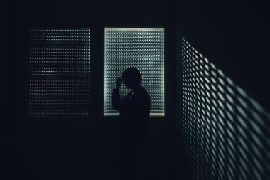 Kapalı pencerenin yanındaki alnına dokunan karamsar kadın silueti izolasyonu, kaygıları, iç gözlem ve duygusal mücadeleyi simgeliyor. Seçici odak.