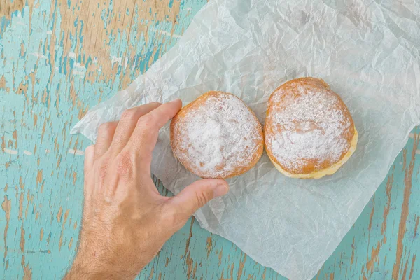 Hand reaches for sweet sugary donut on rustic table — Stock Photo, Image