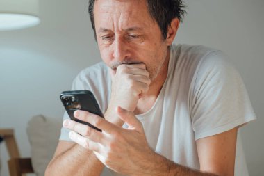 Sıkıcı yetişkin erkek, dikkati dağılmış ve telefonda aylak aylak dolanıyor. Kötü kader kaydırıyor ve boş ifadeyle ve düşük enerji havasıyla oyalanıyor. Seçici odak.