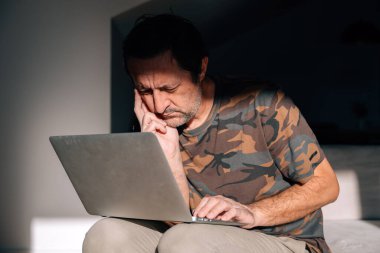 Dizüstü bilgisayarda çalışan olgun bir adam. Görünürde sorunlu ve gergin. Endişeler ve zihinsel zorluklarla boğuşuyor. Seçici odak.