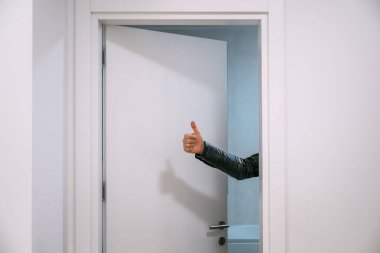 Temiz, modern bir odadaki kapı aralığından kolunu uzatan, görünmeyen birinden bir işaret. Seçici odak.