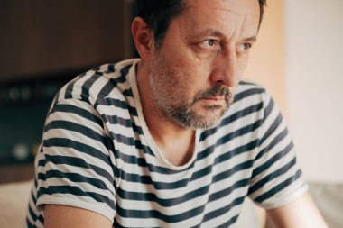 Düşünceli, orta yaşlı, çizgili tişörtlü, stresli, endişeli ve duygusal yorgunluk gösteren bir adam. Seçici odak.