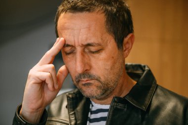 Deri ceketli, unutkan, olgun bir adamın portresi bir şey hatırlamaya çalışırken parmağıyla alnına dokunuyor. Seçici odak.