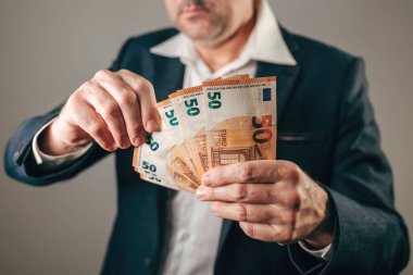 Avrupa para birimi kavramlarında finans ve ödeme, yatırım veya masraf için kameraya doğru 50 Euro tutarında banknot tutan ve yelpazeleyen bir işadamı. Seçici odak.