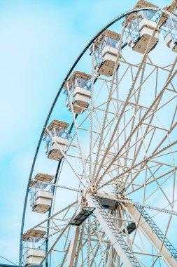 Eğlence parkı ve karnaval konseptleri için açık mavi gökyüzüne karşı beyaz kapalı yolcu kabinleri olan klasik bir dönme dolabın alçak açılı görüntüsü. Seçici odak.