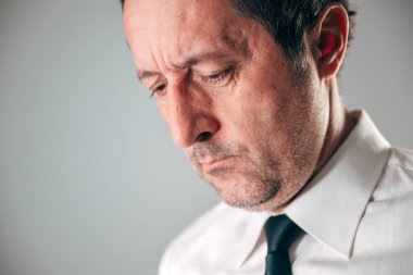 Beyaz gömlekli ve koyu renk kravatlı orta yaşlı bir işadamı yüzünde derin bir hüzün ve hayal kırıklığıyla aşağıya bakıyor. Seçici odak.