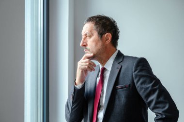 Yorgun ve endişeli işadamı ofis penceresinin önünde dikiliyor, düşüncelere dalmış. Seçici odak.