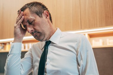 Yıpranmış bir profesyonel alnını elinde dinlendiriyor, hayal kırıklığını, tükenmişliği ve zihinsel yorgunluğu ifade ediyor. Seçici odak.