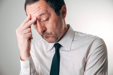 Stresli iş adamı burun köprüsünü çimdikliyor, gözler yorgunluk ve acıdan kapanıyor. Seçici odak.