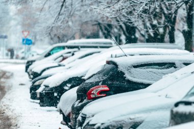 Yerleşim yerlerinde kar yağışı sırasında taze karla kaplı park edilmiş arabalar, açık havada dizilmiş araçlarla soğuk hava kentsel manzarası. Seçici odak.