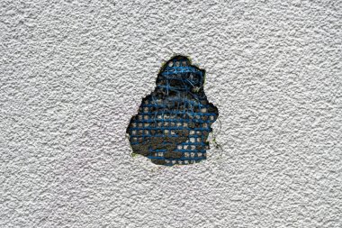 Hasarlı beyaz bina cephesi alçıyla kaplı. Altında mavi destek ağı var. Çürüme, yaşlanma ve inşaat detaylarını gösteriyor..