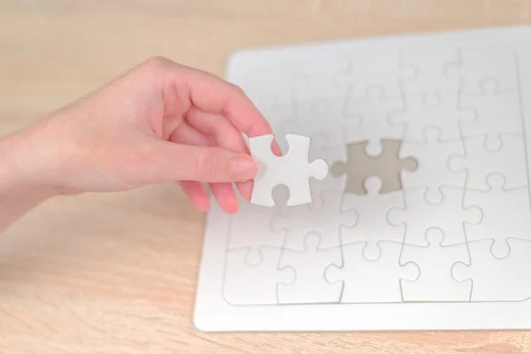 Female hand putting a missing piece into jigsaw puzzle — Stock Photo, Image