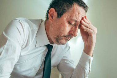 Stresli iş adamı, elleri alnında, iş yerinde zihinsel yorgunluk ve tükenmişlik gösteriyor. Seçici odak.