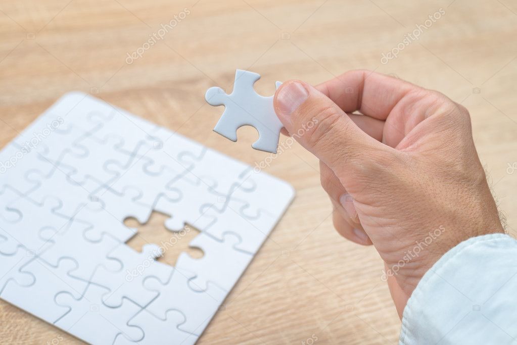 Businessman hand putting a missing piece into jigsaw puzzle