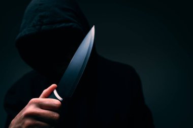 Siyah elbiseli kapüşonlu bir şahıs, yüzü tamamen karanlık, büyük bir mutfak bıçağı tutuyor, seçici bir odak noktası var.