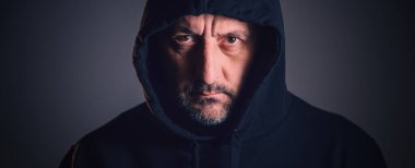 Orta yaşlı bir adamın portresi, kısa sakallı ve yıpranmış yüzlü koyu renk kapüşonlu bir kapüşonlu giymiş, çatık kaşlı ve yoğun bakışlı. Seçici odak.