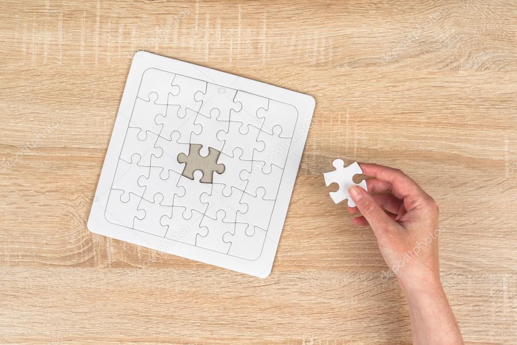 Female hand putting a missing piece into jigsaw puzzle