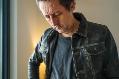 Deri ceketli düşünceli bir adam üzüntüyle, seçici bir dikkatle aşağıya bakıyor.