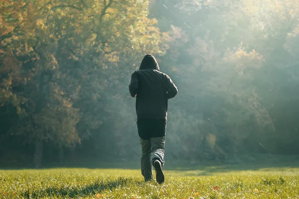 Hooded man jogging in the park in early autumn morning — Stock Photo, Image