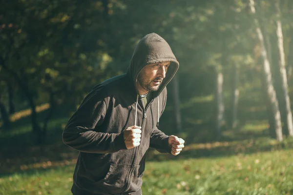 Hombre encapuchado corriendo en el parque en la mañana de otoño — Foto de Stock