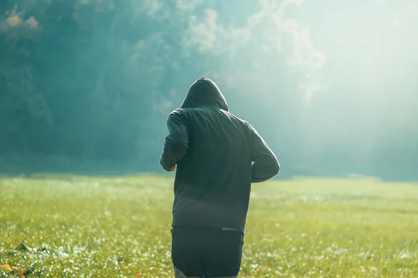 Hooded man jogga i parken i tidig höst morgon — Stockfoto