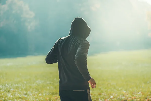 Muž v kapuci běhání v parku v ranní podzimní — Stock fotografie