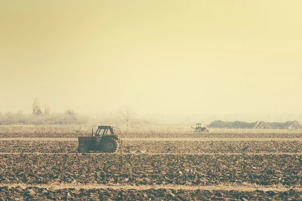 Retro toned tractors on arable field — Stock Photo, Image