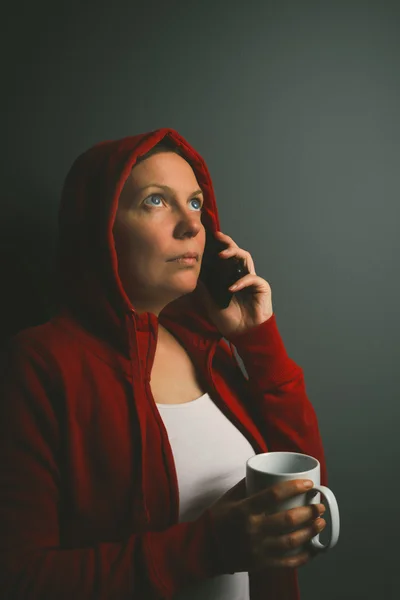 Hermosa mujer con capucha roja bebiendo café y utilizando el teléfono móvil —  Fotos de Stock