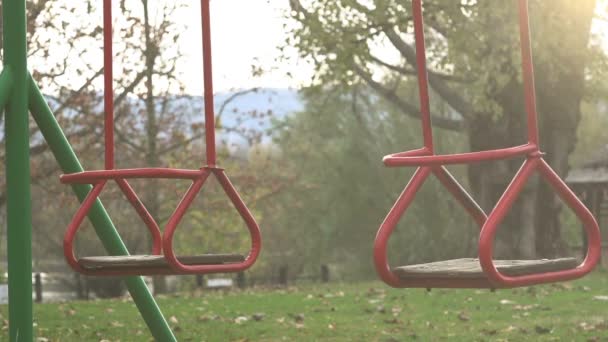 Empty red swing seat swaying in park playground — Stock Video