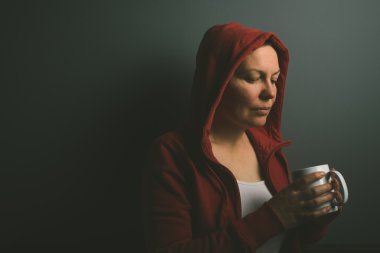 Beautiful red hooded lonely woman drinking coffee