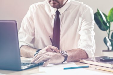 Not yazmak ve Ofis Masası dizüstü bilgisayar kullanarak bir işadamı