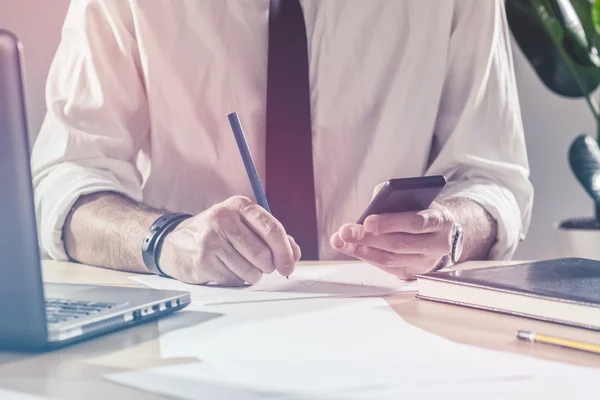 Geschäftsmann schreibt am Schreibtisch Notizen vom Handy — Stockfoto