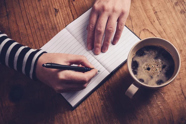 Mujer bebiendo café y escribiendo una nota de diario — Foto de Stock