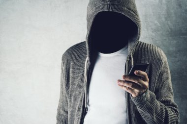 Faceless hooded person using mobile phone, identity theft concep clipart