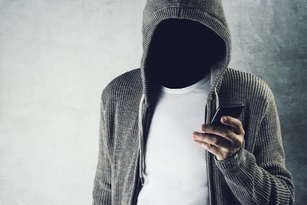 Faceless hooded person using mobile phone, identity theft concep — Stock Photo, Image