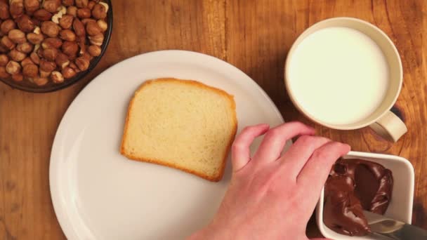 Woman spreading hazelnut nougat cream over bread slice — Stock Video