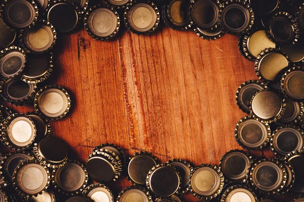 Beer bottle caps frame over wooden background — Stock Photo, Image