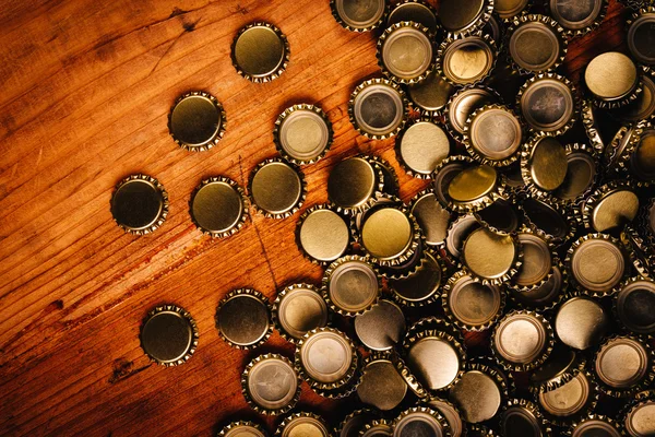 Large pile of beer bottle caps on wooden desk — Stock Photo, Image